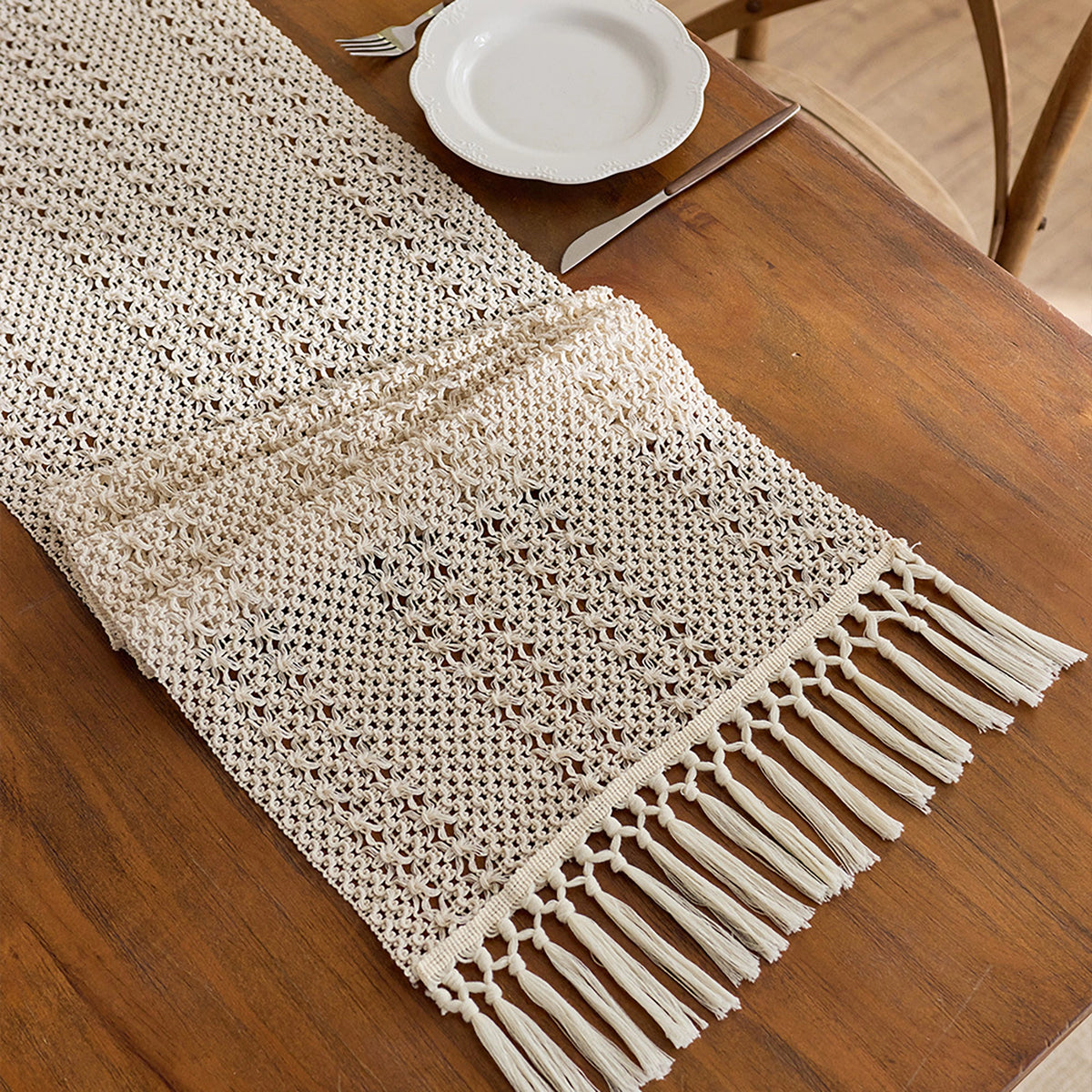 Beige crocheted table runner with fringe on a wooden table.