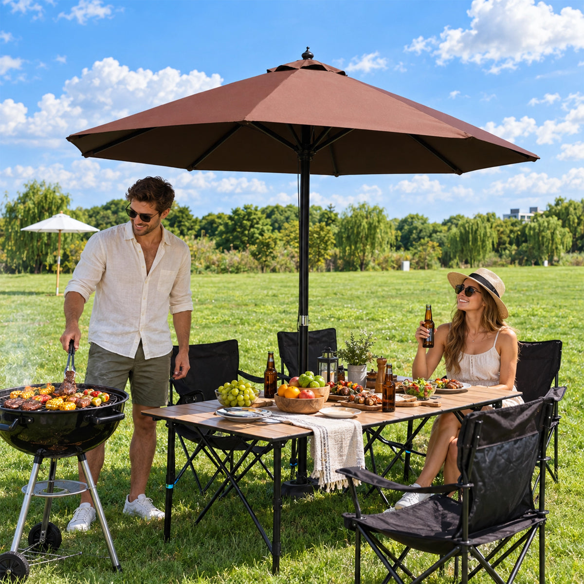 Folding camping table set for a picnic under a patio umbrella next to a grill